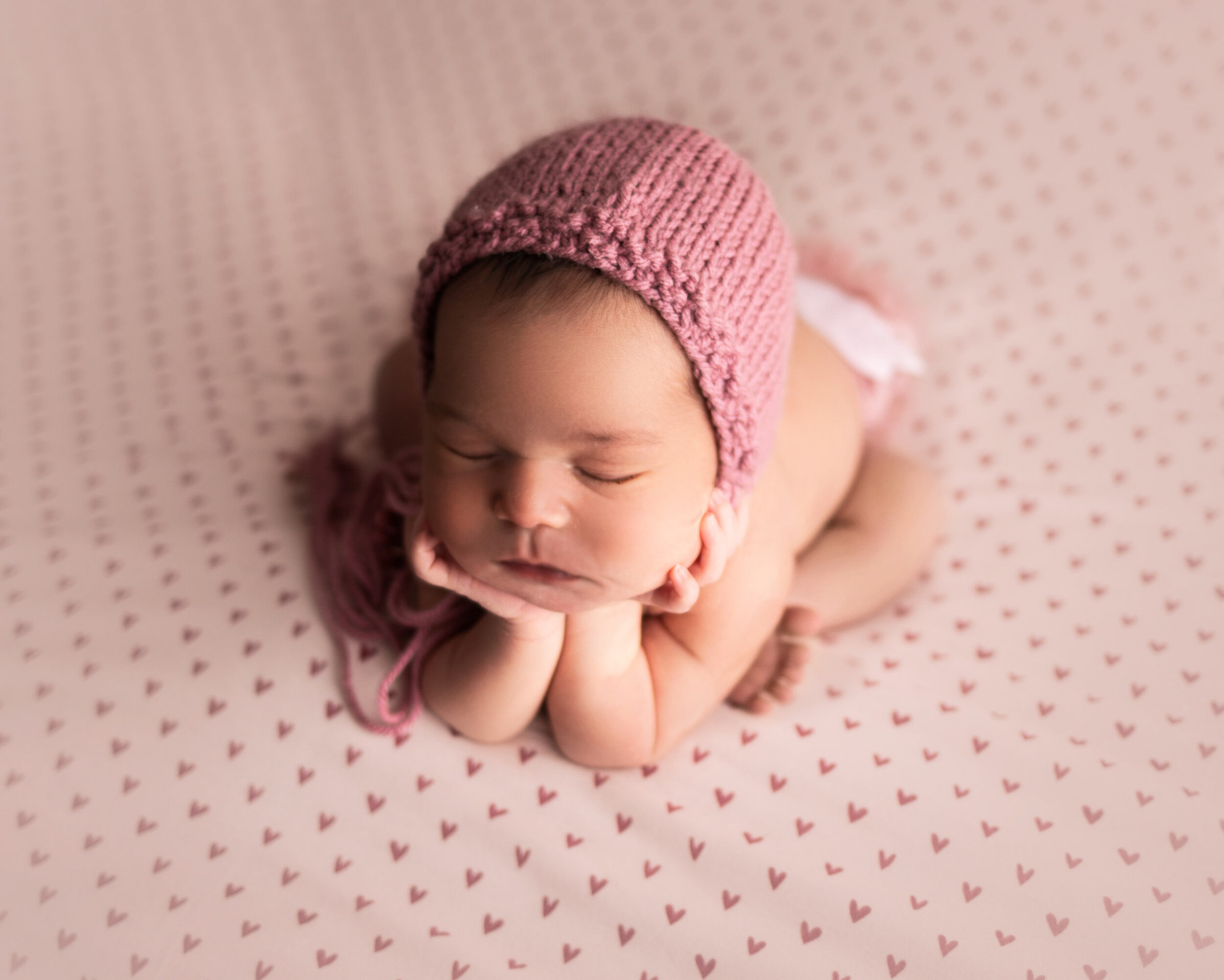 newborn girl on heart backdrop in froggy pose with pink bonnet by baby photographer in Minneapolis mn