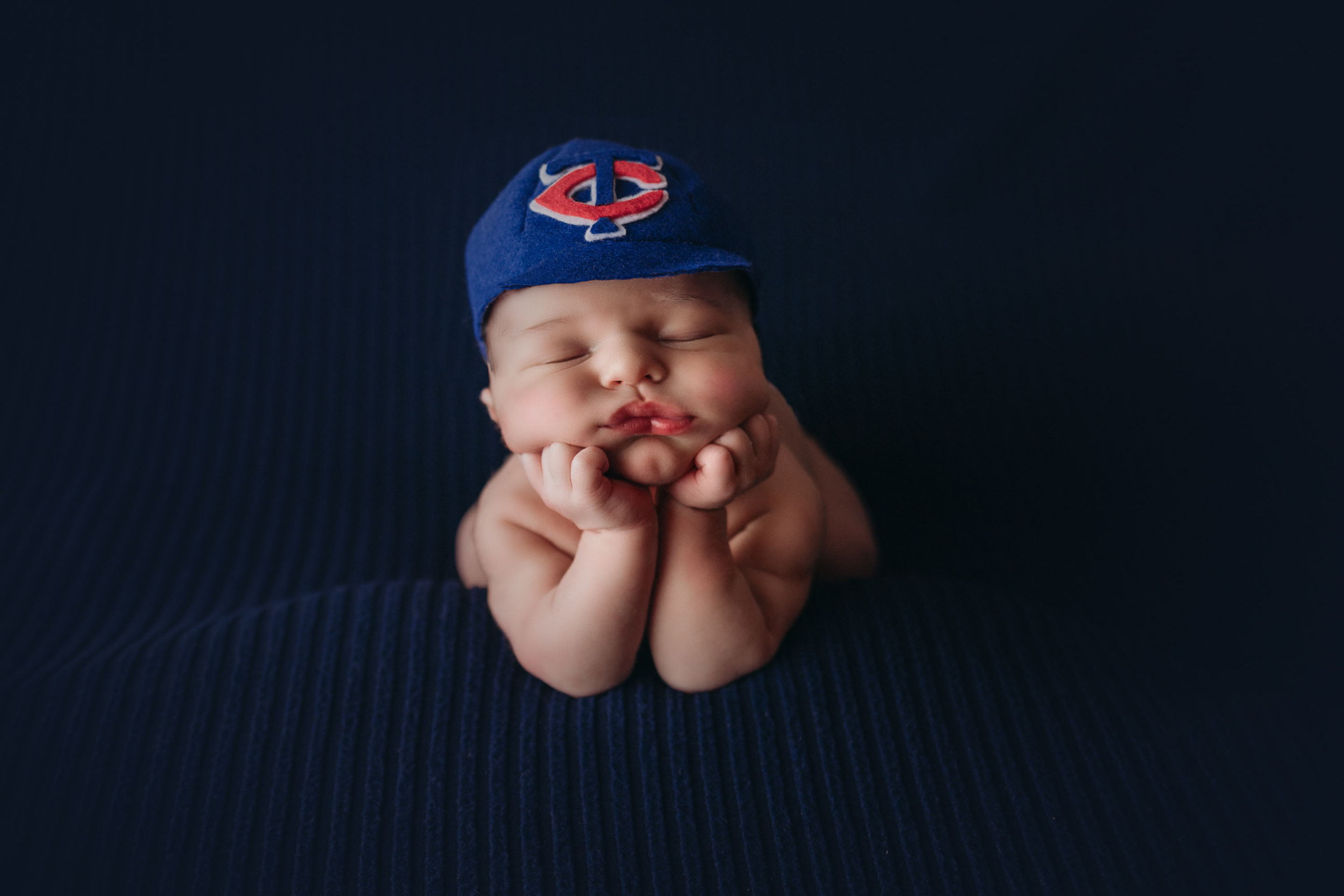 baby boy in froggy pose in twins baseball hat for newborn session by professional photographer in minneapolis mn