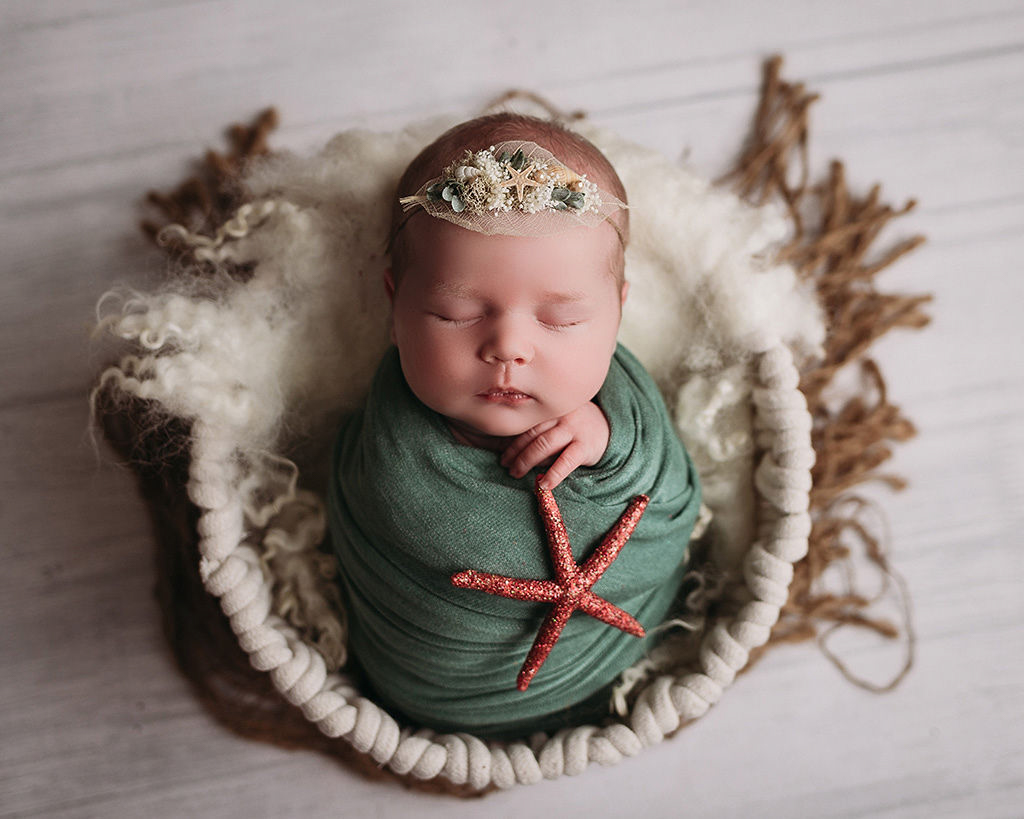 baby girl in sage wrap with orange starfish and seashell headband in boho basket newborn photographer minneapolis