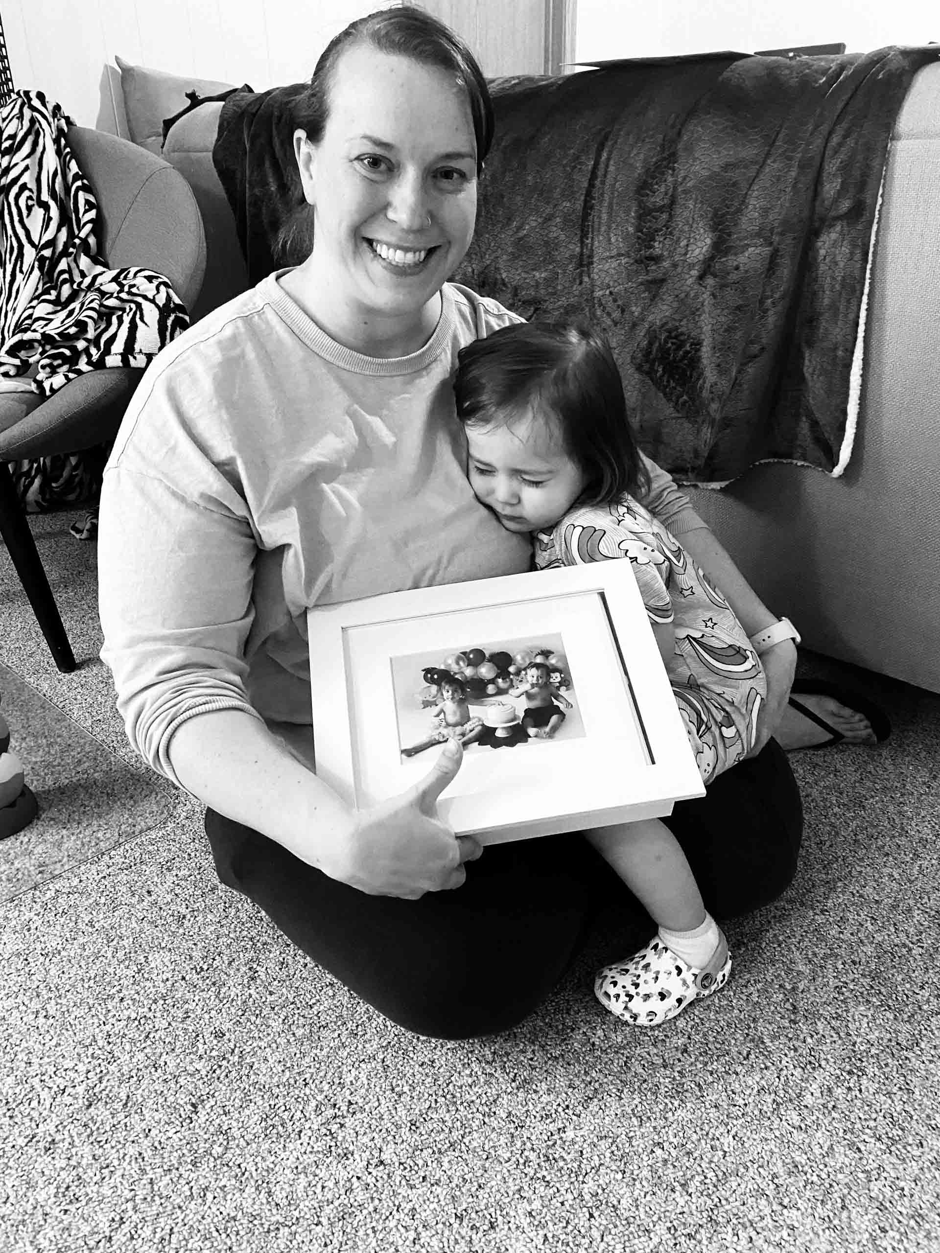 mom and baby girl with folio prints and folio box after reveal wall minneapolis kids photography