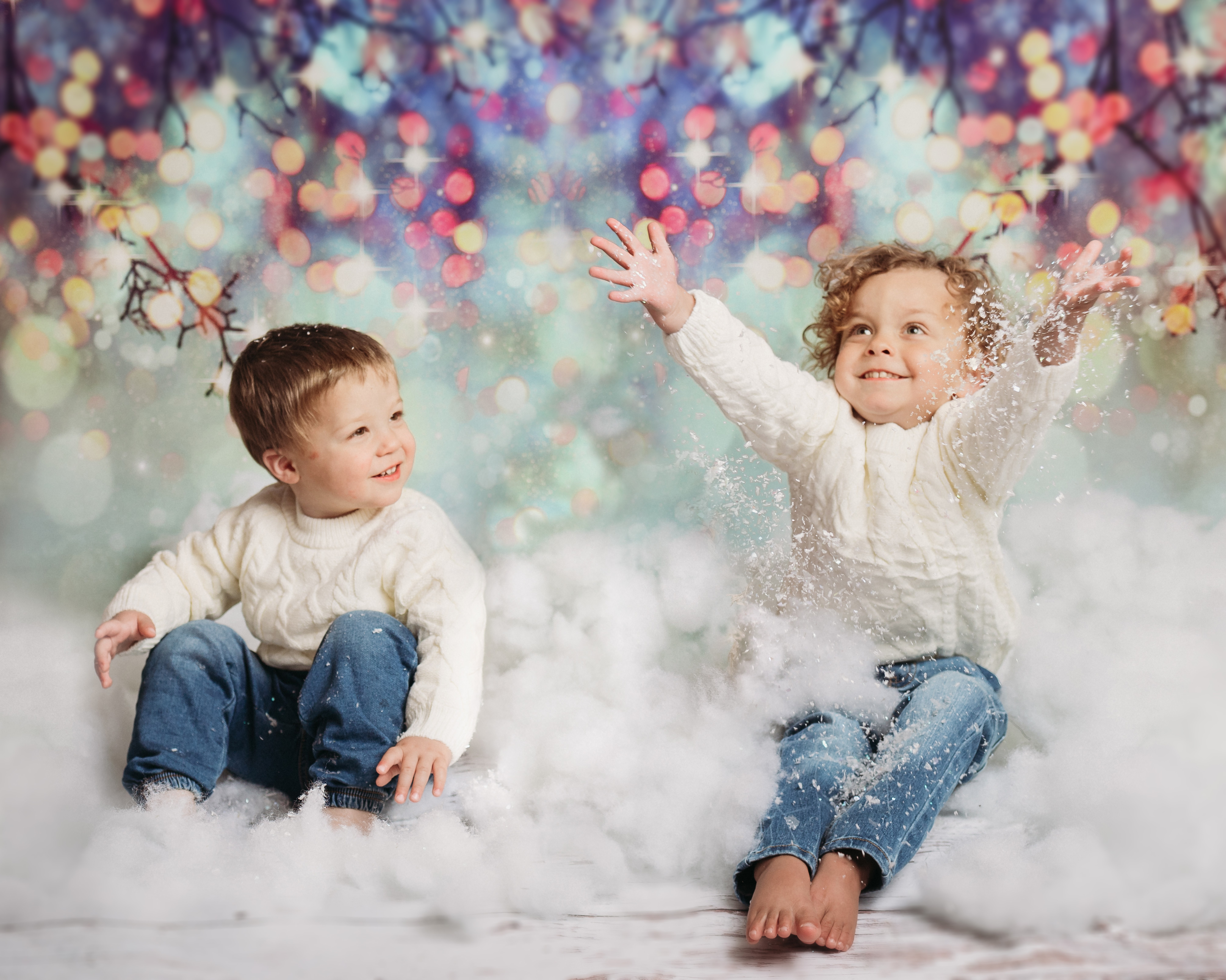 holiday photoshoot with two toddler boys in jeans and white sweaters throwing snow in front of bokeh backdrop for minneapolis family session