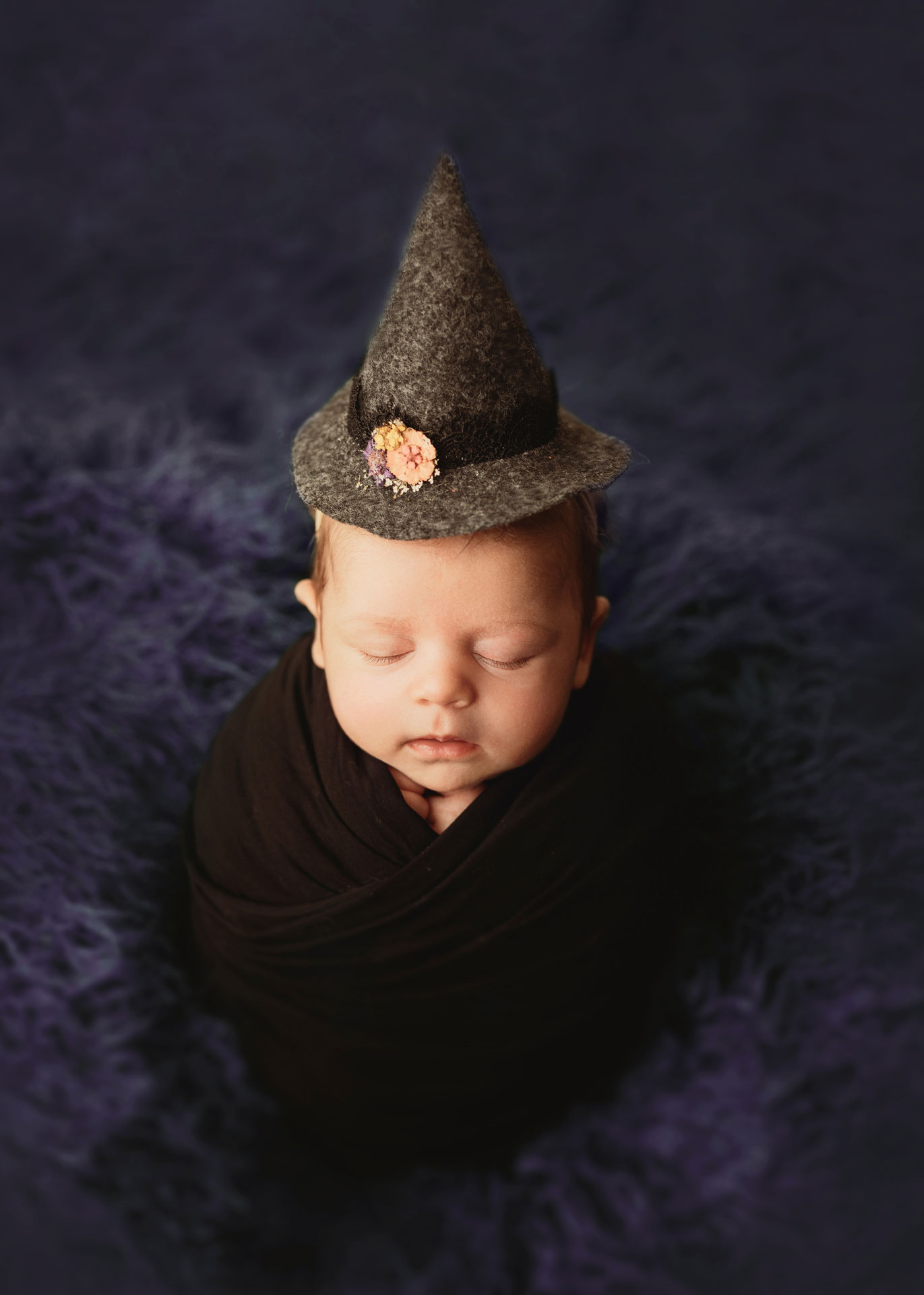 newborn girl in gray witch hat with orange yellow and purple flowers on amethyst flokati minneapolis minnesota newborn photographer